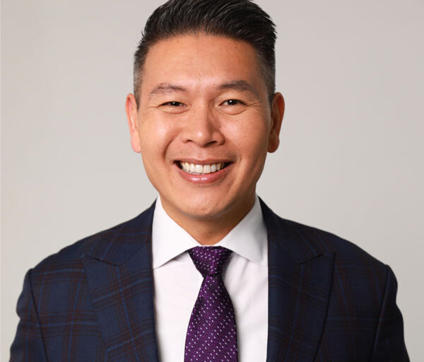 Headshot of Derek Tran in a patterned blue blazer with a purple and white polka dot tie.
