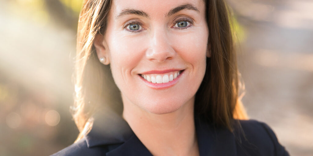 Headshot of Missy Cotter Smasal smiling in a black blazer with long straight hair and a glowy natural scenery.