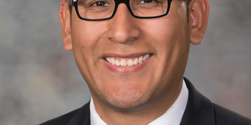 Headshot of Tony Vargas smiling in a black blazer and a white shirt with polka dot red and white tie.