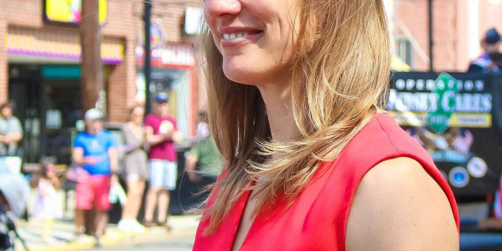 Susan Altman in a red top smiling off into the distance while holding something in her hand.