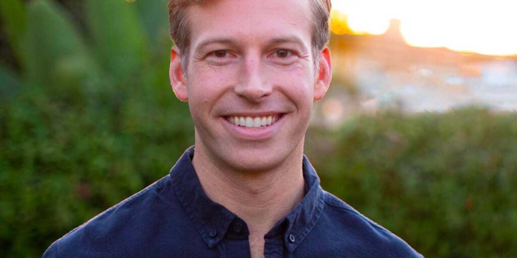 Headshot of Will Rollins with an organic nature background and a blue shirt.