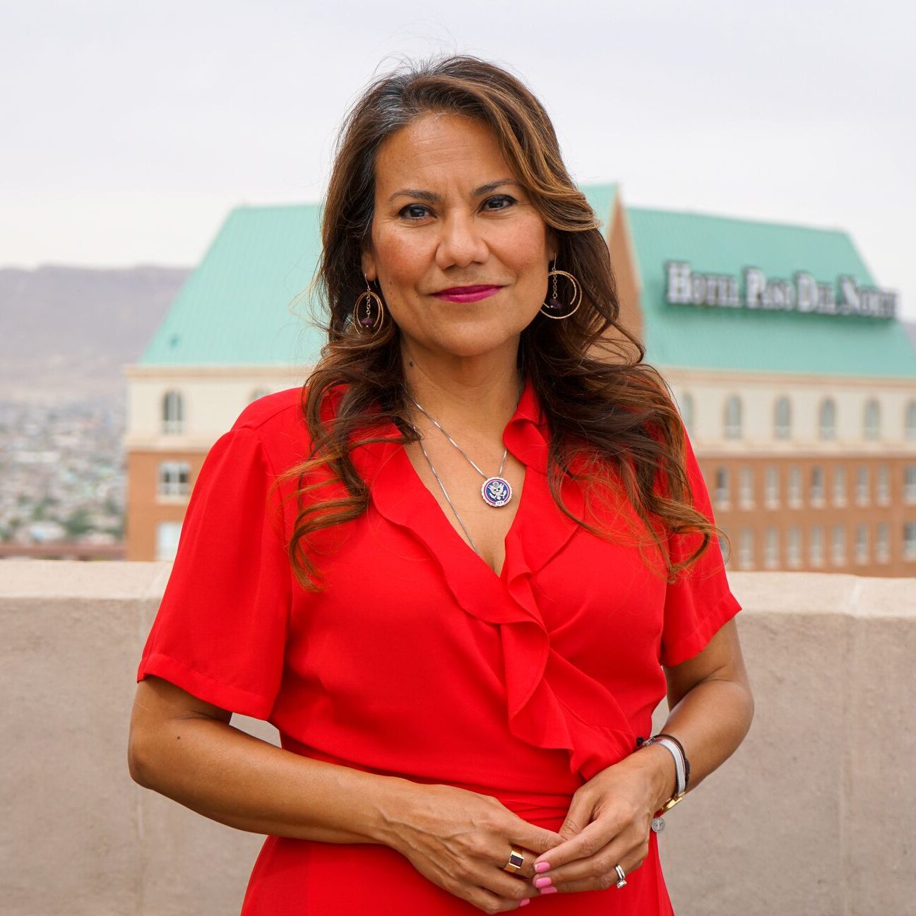Veronica Escobar is pictured standing outdoors in a red dress with mountains in the background.