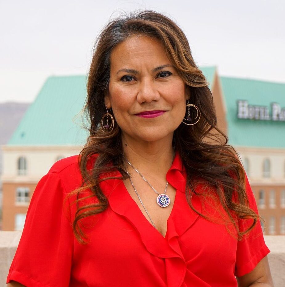 Veronica Escobar is pictured standing outdoors in a red dress with mountains in the background.