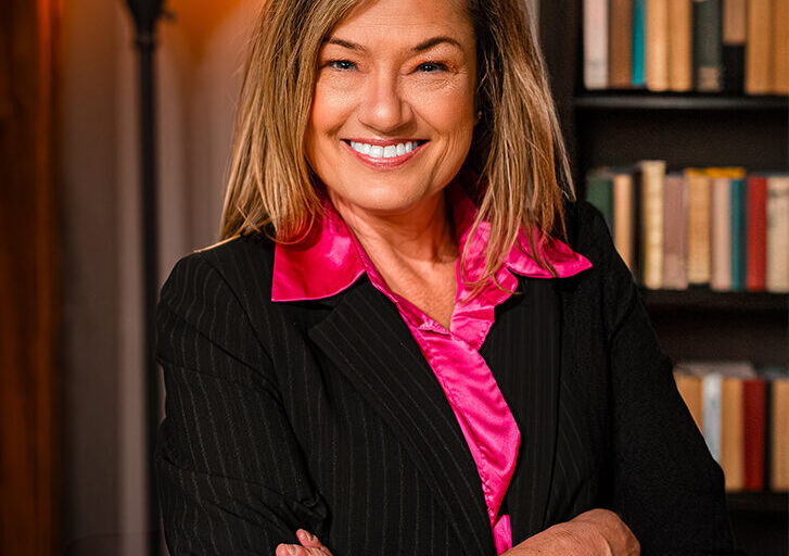 Sarah Corkey smiling in a black blazer and a hot pink shirt in a library.