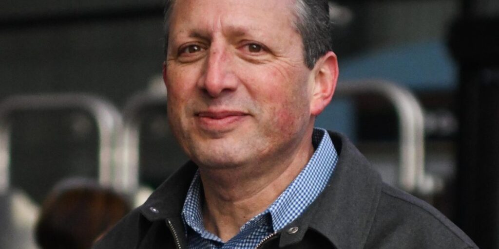 Brad Lander portrait. He's smiling at the camera wearing a grey jacket and blue collared shirt.