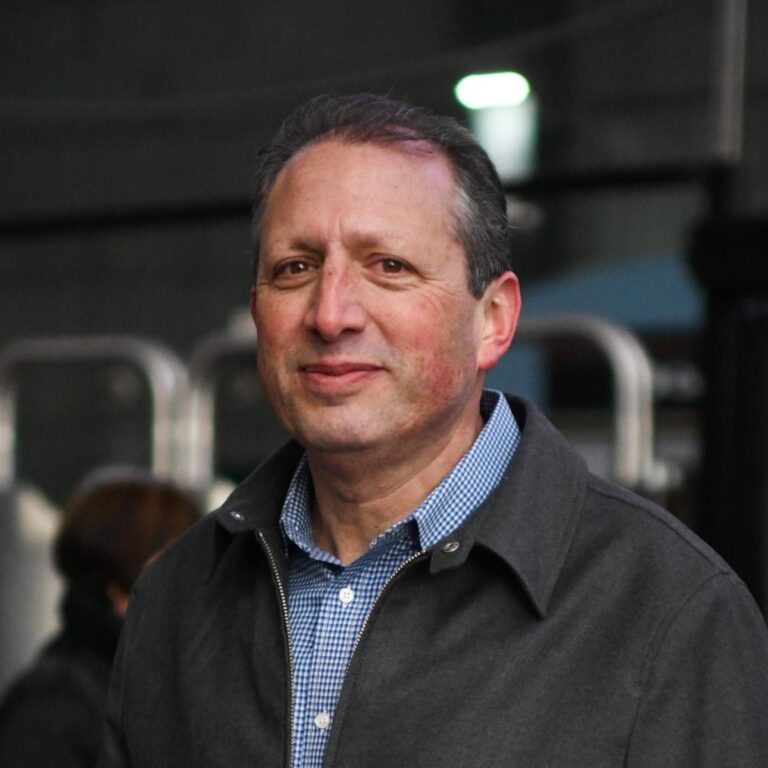 Brad Lander portrait. He's smiling at the camera wearing a grey jacket and blue collared shirt.