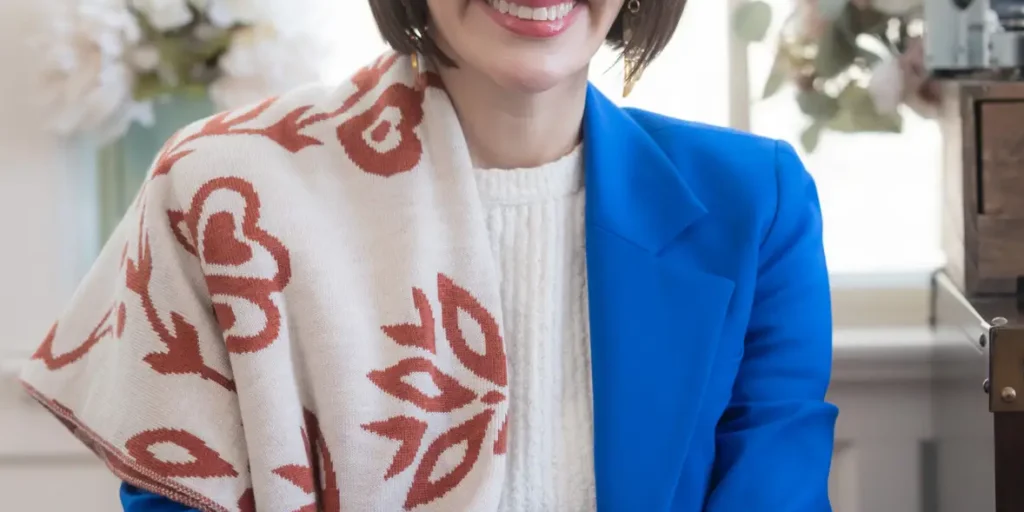 This is an image of Peggy Flanagan, candidate for Minnesota Senate. She is pictured in a blue suit sitting on a chair in a home.