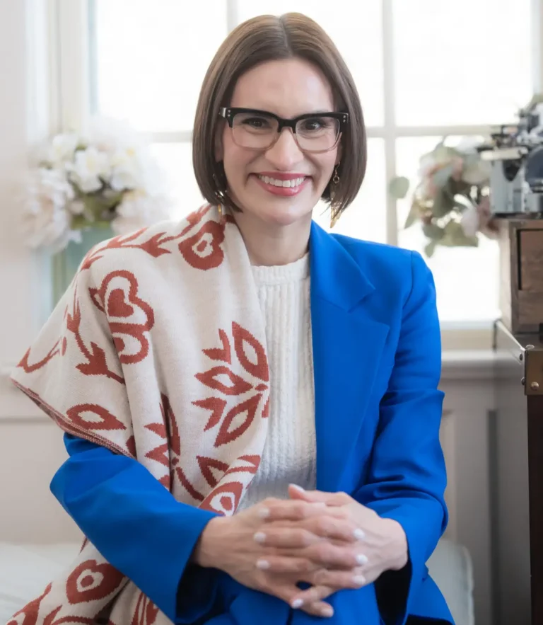 This is an image of Peggy Flanagan, candidate for Minnesota Senate. She is pictured in a blue suit sitting on a chair in a home.