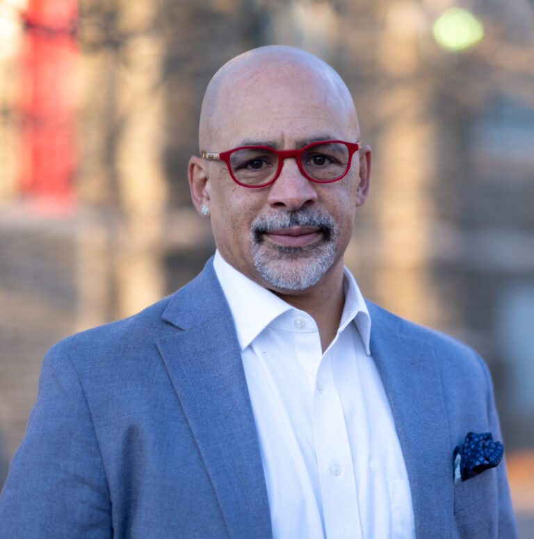 This is an image of Chris Rabb, candidate for Pennsylvania's 3rd Congressional District. He is pictured in a blue suit in front of a building.