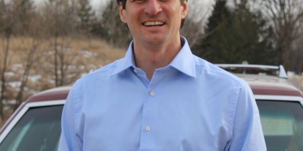 This is an image of Matt Little, candidate for Minnesota's 2nd Congressional District. He is pictured in a blue shirt in front of a red car.