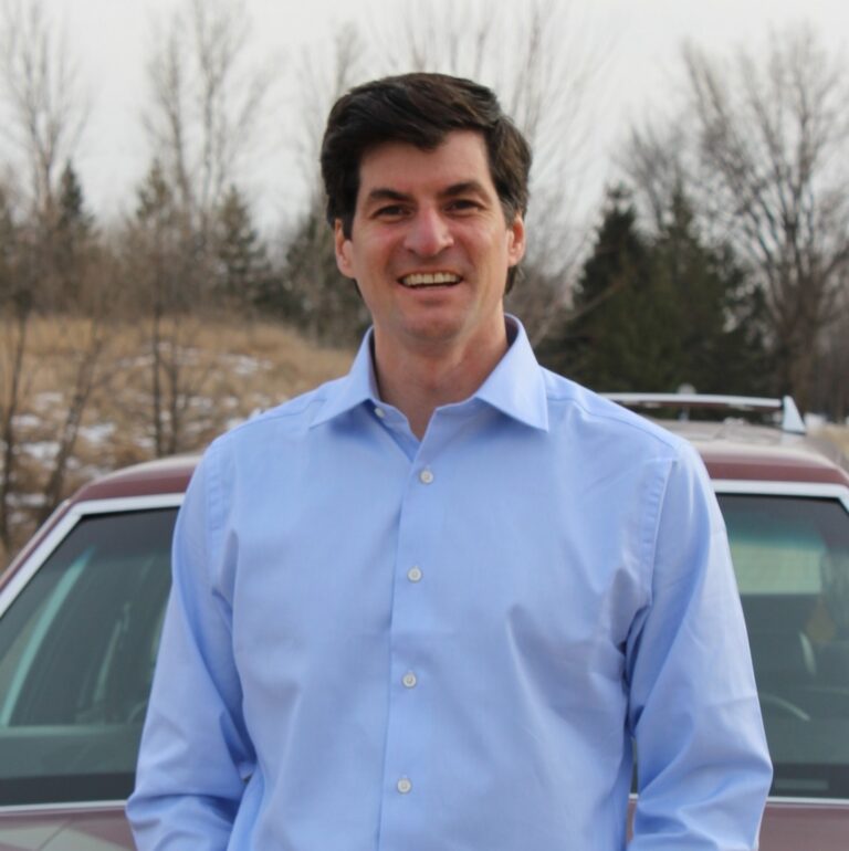 This is an image of Matt Little, candidate for Minnesota's 2nd Congressional District. He is pictured in a blue shirt in front of a red car.