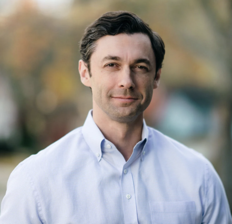 This is an image of Jon Ossoff, candidate for Georgia Senate. He is pictured in a blue shirt in front of trees.