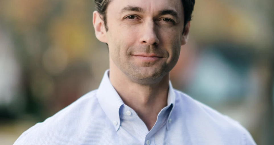 This is an image of Jon Ossoff, candidate for Georgia Senate. He is pictured in a blue shirt in front of trees.