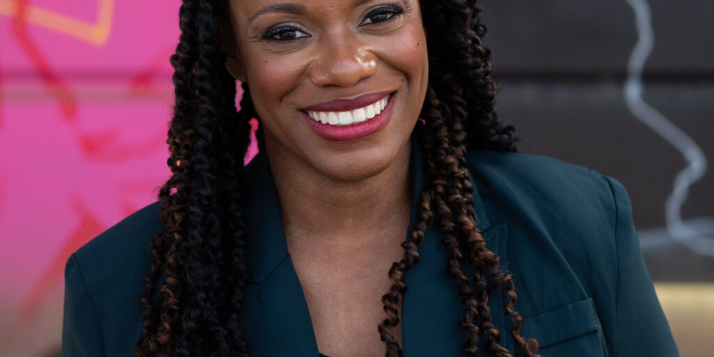 This is an image of Summer Lee, candidate for Pennsylvania's 12th Congressional District. She is pictured in a blue suit in front of a pink mural.