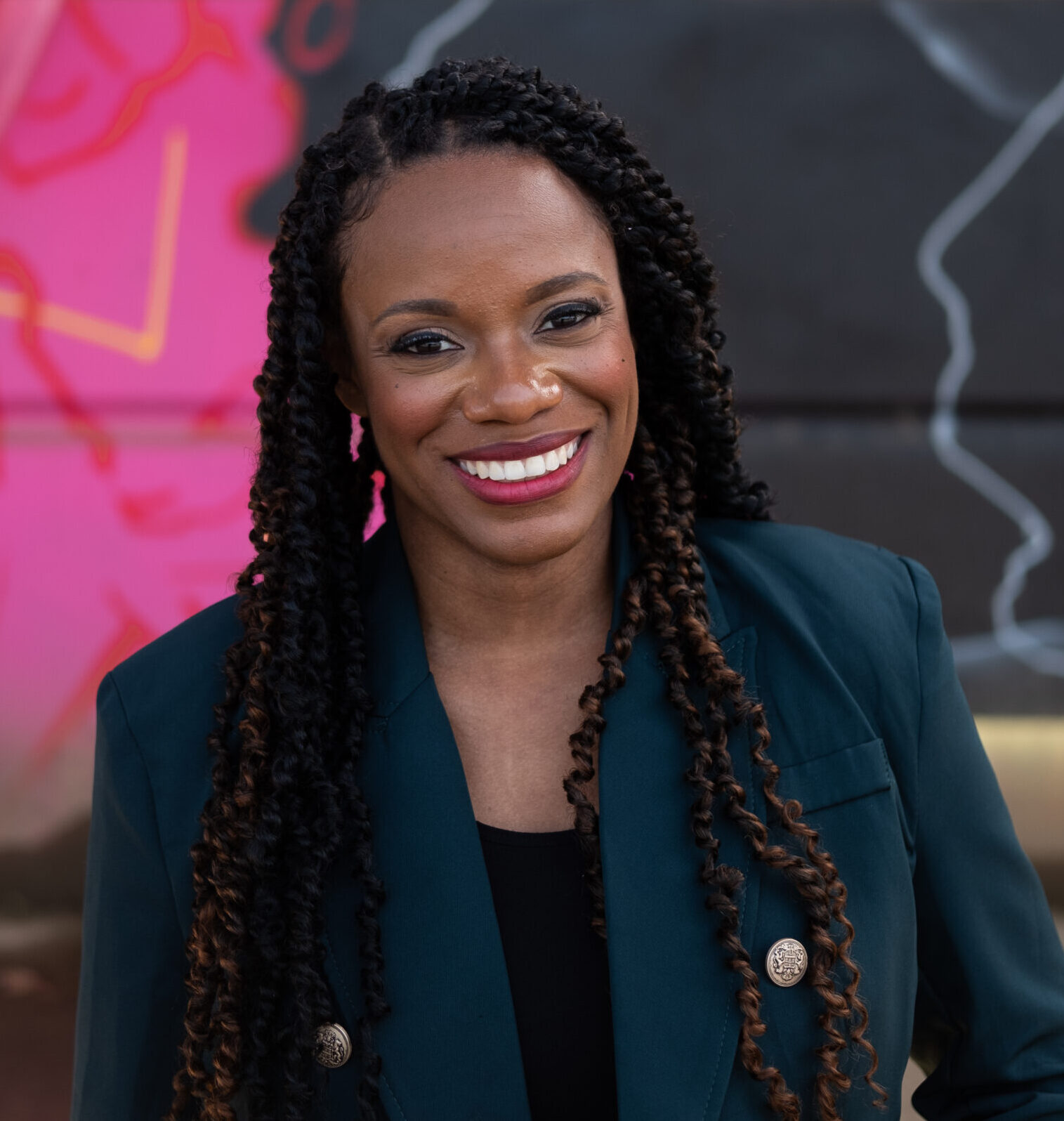 This is an image of Summer Lee, candidate for Pennsylvania's 12th Congressional District. She is pictured in a blue suit in front of a pink mural.