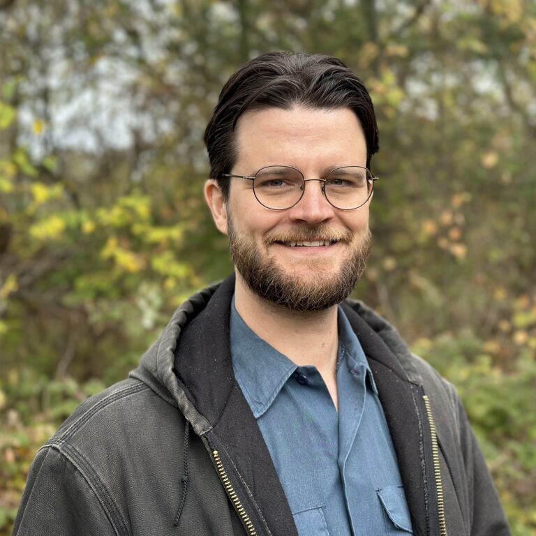 This is an image of William Lawrence, candidate for Michigan's 7th Congressional District. He is pictured in a blue shirt and gray hoodie in front of a forest.