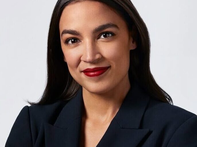 This is an image of Alexandria Ocasio-Cortez, candidate for New York's 14th Congressional District. She is pictured in a black blazer with her arms crossed in front of an all white background.