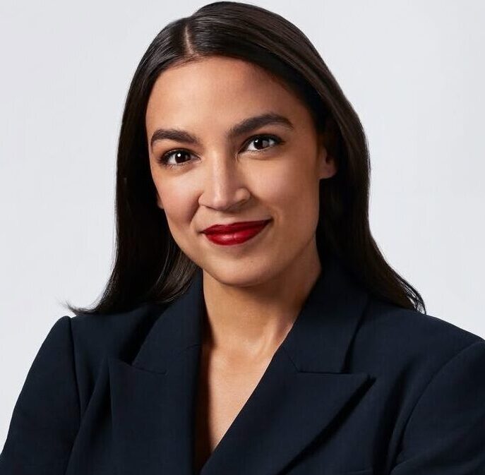 This is an image of Alexandria Ocasio-Cortez, candidate for New York's 14th Congressional District. She is pictured in a black blazer with her arms crossed in front of an all white background.