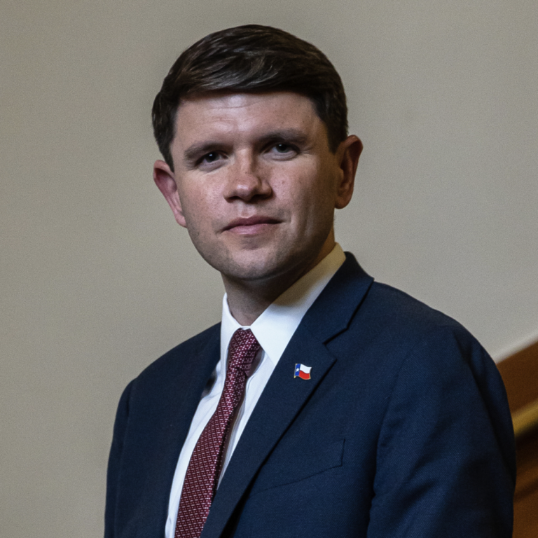 This is an image of James Talarico, candidate for Texas Senate. He is pictured in a blue suit with a white shirt and red tie standing on a brown staircase.