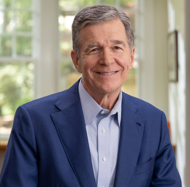This is an image of Roy Cooper, candidate for North Carolina Senate. He is pictured in a blue suit with a blue shirt in a home.