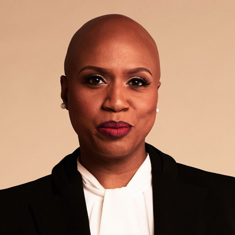 This is an image of Ayanna Pressley, candidate for Massachusetts's 7th Congressional District. She is pictured in a black blazer with a white shirt in front of a bronze background.