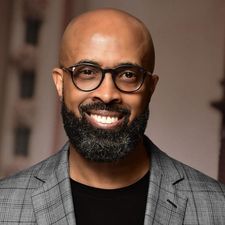 This is an image of Rev. Frederick D. Haynes III, candidate for Texas's 30th Congressional District. He is pictured in a striped gray suit with a black shirt in front of a brown background.