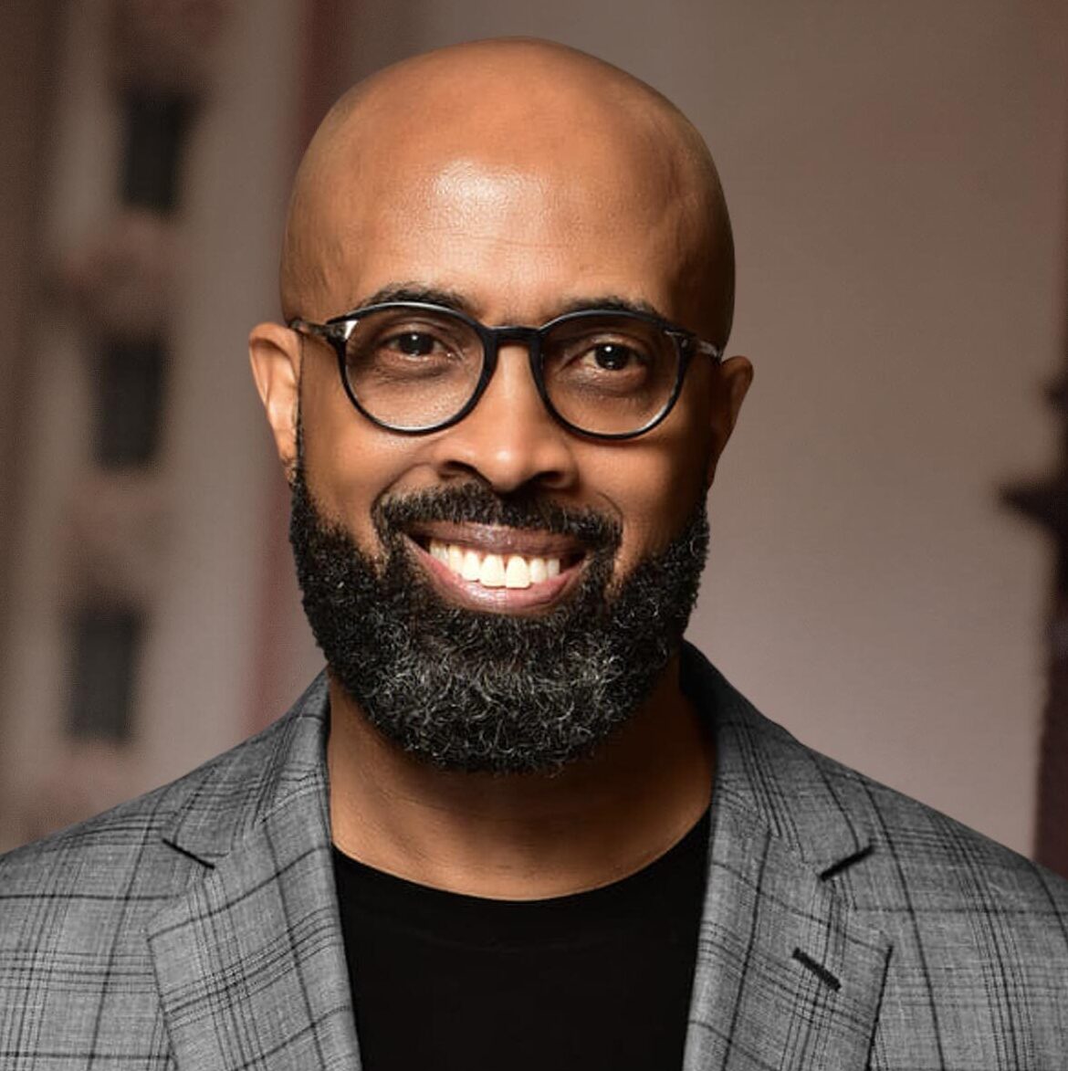 This is an image of Rev. Frederick D. Haynes III, candidate for Texas's 30th Congressional District. He is pictured in a striped gray suit with a black shirt in front of a brown background.