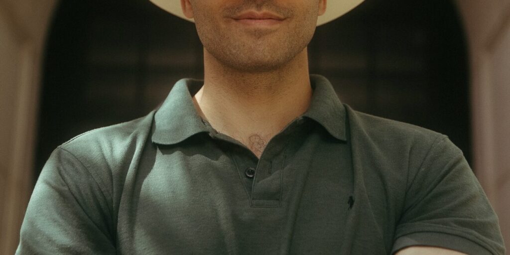 This is an image of Manny Rutinel, candidate for Colorado's 8th Congressional District. He is pictured in a green polo shirt with a cream color cowboy hat standing with his arms crossed in front of a building.
