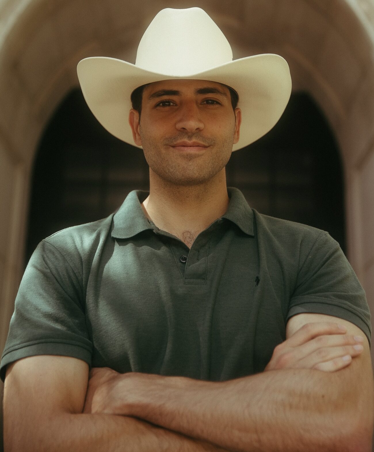 This is an image of Manny Rutinel, candidate for Colorado's 8th Congressional District. He is pictured in a green polo shirt with a cream color cowboy hat standing with his arms crossed in front of a building.