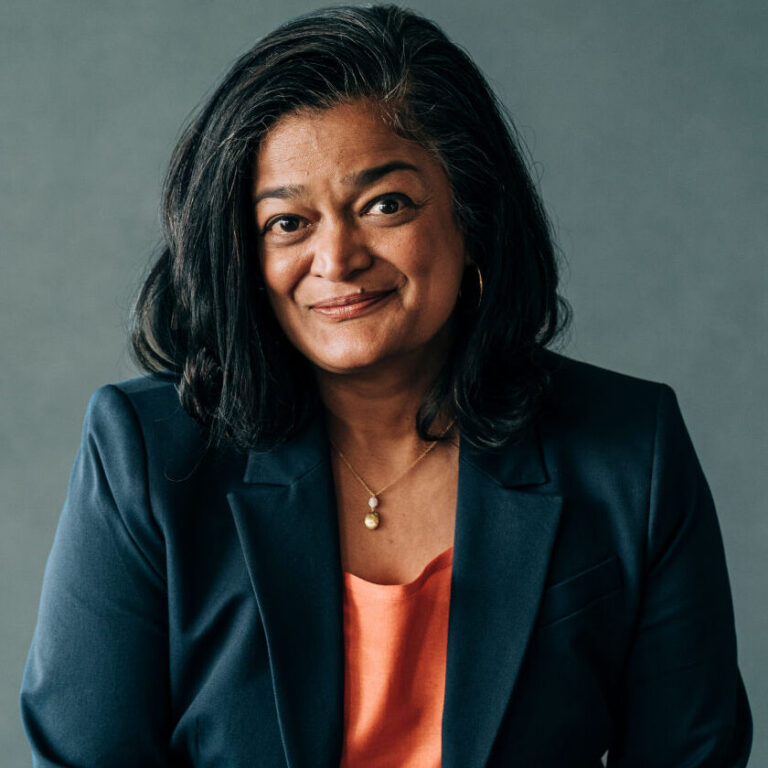 This is an image of Pramila Jayapal, candidate for Washington's 7th Congressional District. She is pictured in a black suit with a peach shirt in front of a gray wall.