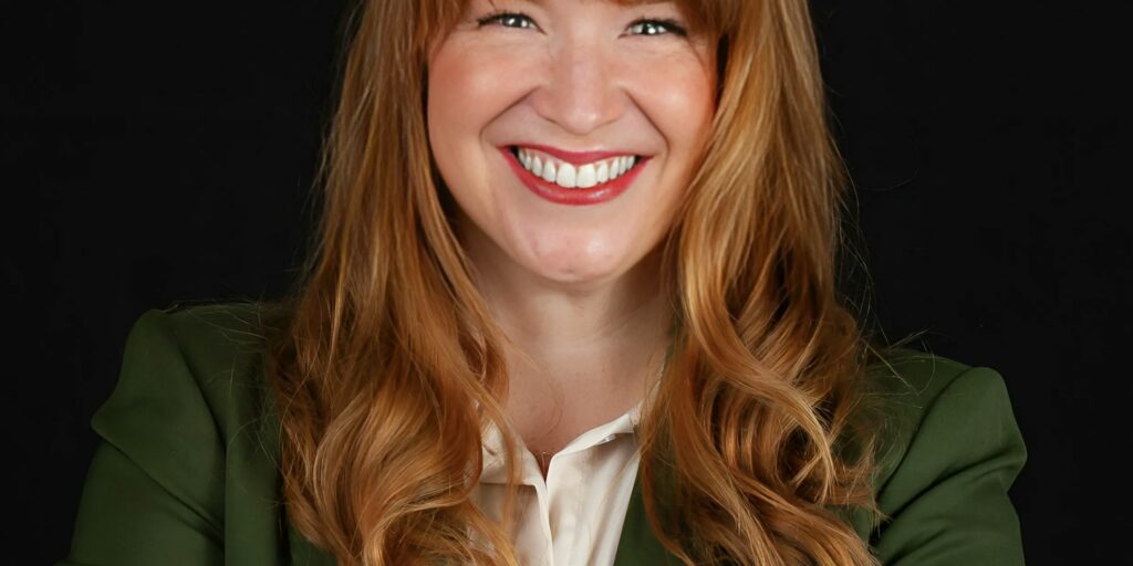 This is an image of Lindsay James, candidate for Iowa's 2nd Congressional District. She is pictured in a green suit with a white shirt in front of a black background.